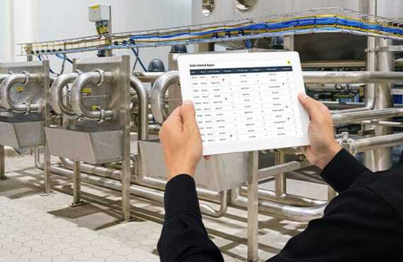 A facilities manager in a factory using a tablet to operate digital industrial control systems.