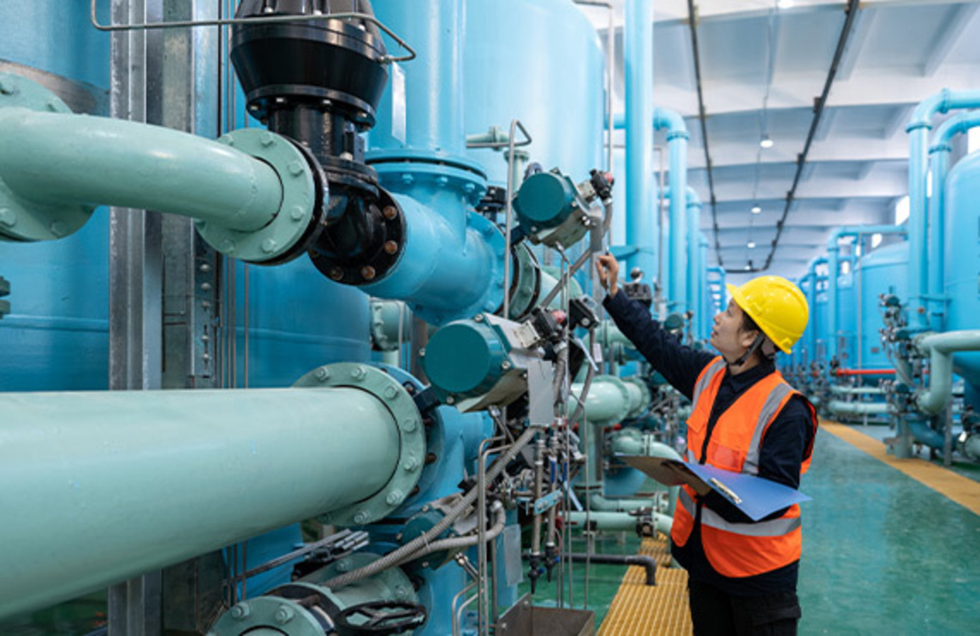 A worker inspecting pipes in a water treatment plant in an industrial control system environment.
