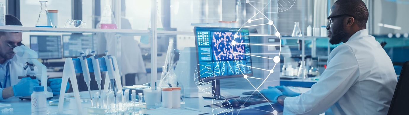 A life sciences manufacturing worker wearing glasses and a white lab coat sitting at a computer.