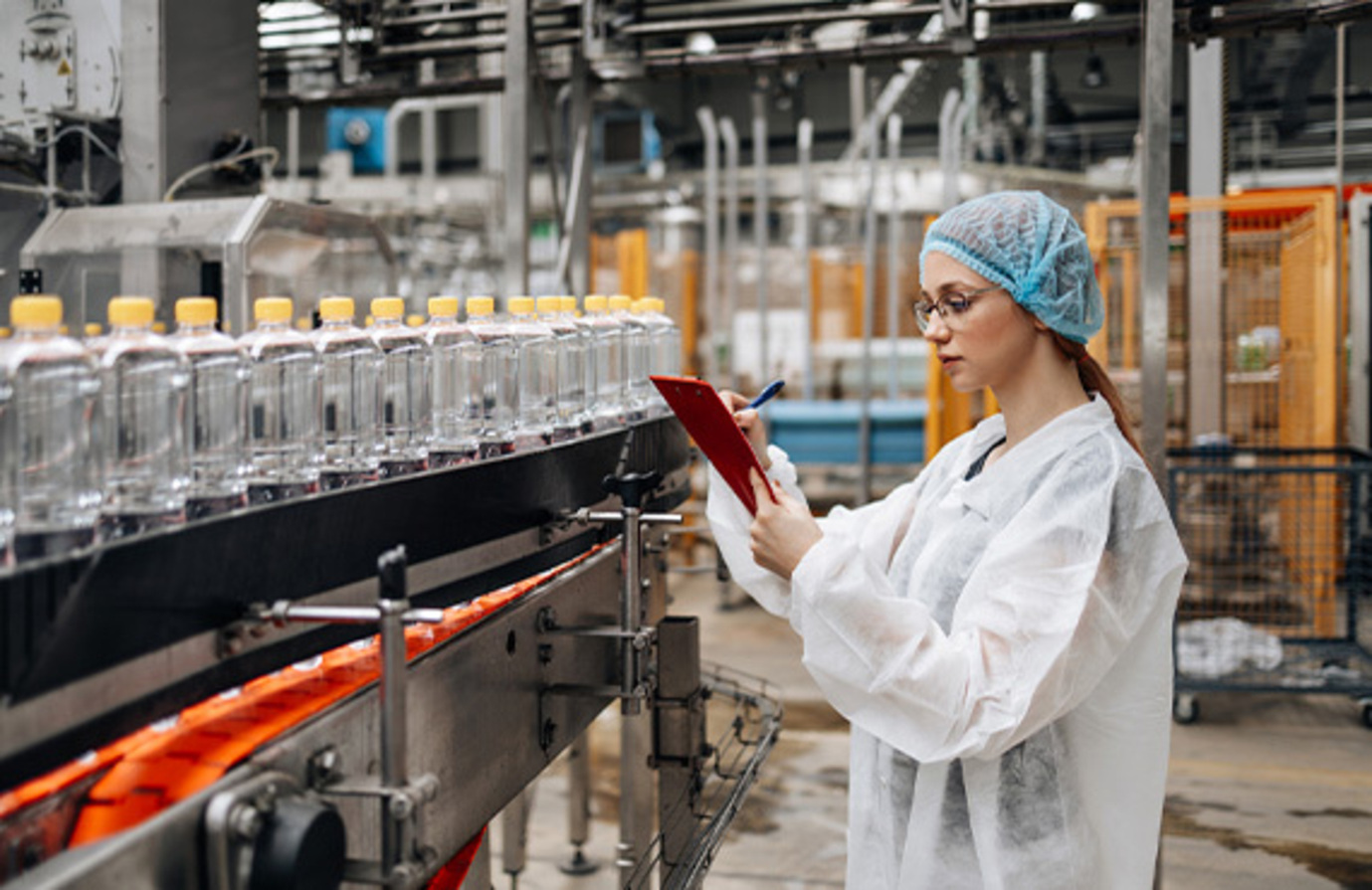 Female worker inspecting bottles in a food and beverage factory, ensuring quality control in the manufacturing process.
