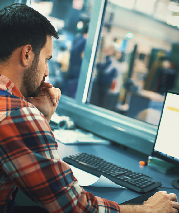 Plant worker in a control room wearing a flannel shirt and sitting at a computer.