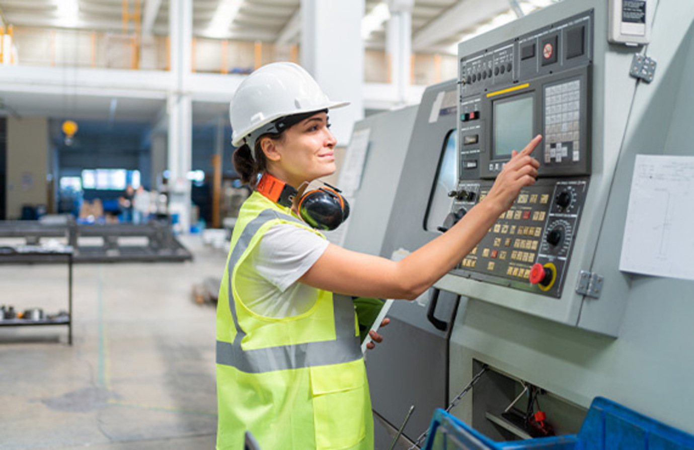 Female worker operating manufacturing industrial controls at machine.
