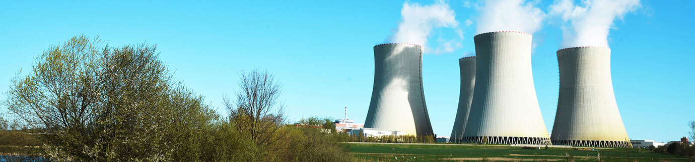 Image of a nuclear energy power plant against a blue sky with green fields in the foreground.