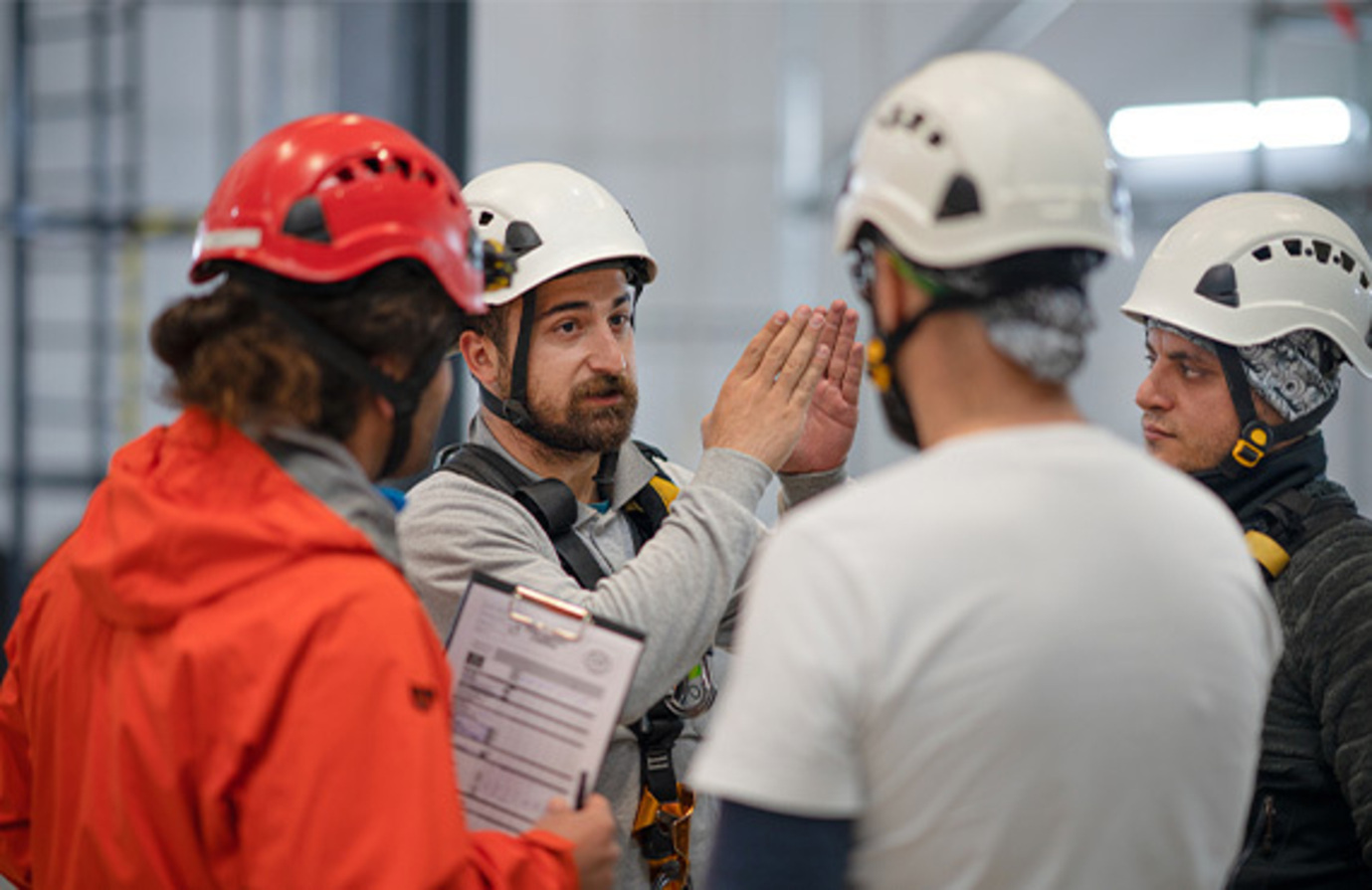 Three men in a factory listen to an instructor engaged who is discussing customized training programs for their manufacturing facility.
