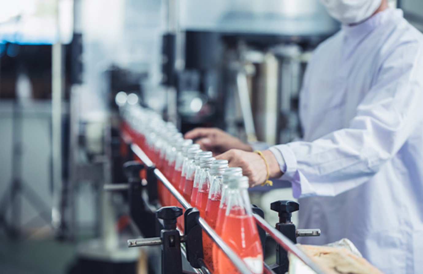 In a quality control area, a worker in a white coat organizes bottles on a conveyor belt for food and beverage production.