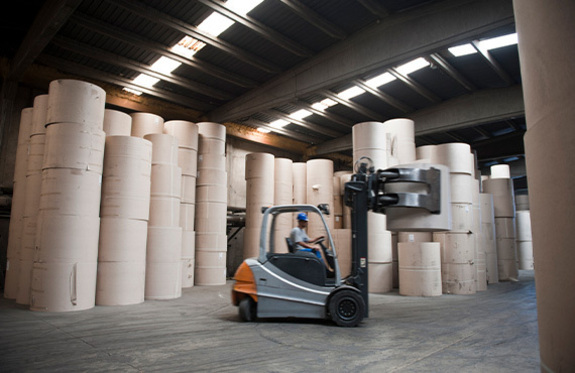 A forklift truck in a warehouse with paper rolls, used for machine condition monitoring in the paper manufacturing industry.