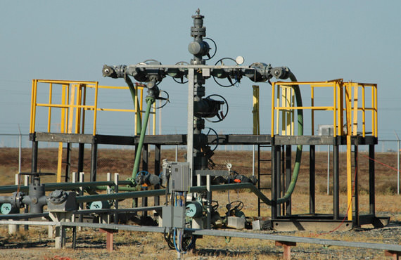 An industrial wellhead with yellow safety rails and piping under a blue sky